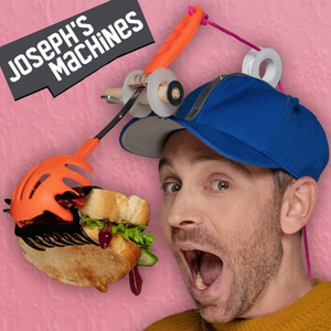 Close-up photo of a man's face and neck. He's wearing a blue ball cap on which are attached 2 pulleys through which red yarn is threaded and connected to an orange, plastic, pronged cooking spoon, connected to a black hair clip that is holding a sandwich with dripping ketchup and lettuce. His mouth is open and he is trying to eat the sandwich as his contraption stuffs it in his mouth. 