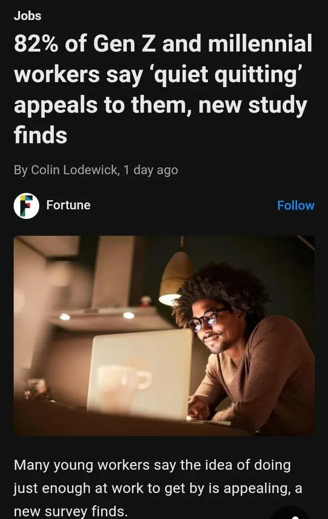 Photo of a young Black man with curly hair and glasses smiling as he looks at a laptop screen in his home