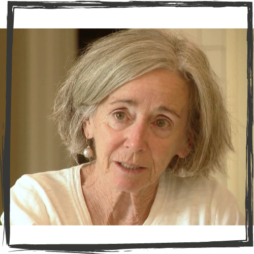 Photo of an older white woman w/chin length gray hair, white dangling earrings and wearing a white shirt