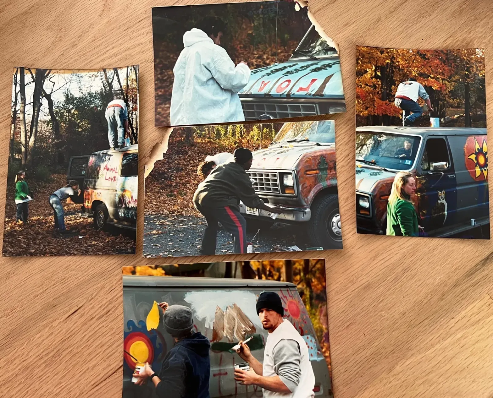 Six restored photos of men and women in a forested area repainting a Ford van with images of flowers and mountains, probably from the 1970s