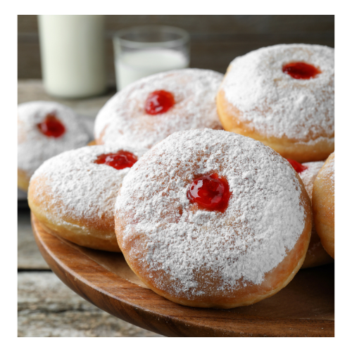 A wood platter of jelly donuts covered in powdered sugar & topped w/a dollop of red jelly on top. In the background is a glass of milk