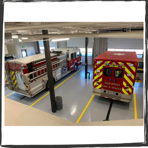 Photo inside a fire station with a fire truck parked on the left and an ambulance on the right.