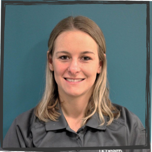 A young, white woman with shoulder-length blonde hair wears a gray polo shirt. She is smiling