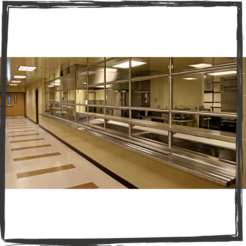 A long hallway is reflected in a wall of windows. The floor is punctuated by narrow, rectangular, brown tiles