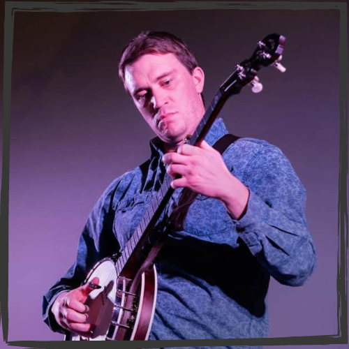 A white man wearing a blue shirt plays a banjo on stage