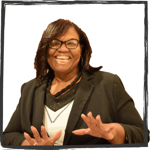 A Photo of a Black woman w/shoulder-length black hair, glasses & wearing a suit smiles broadly