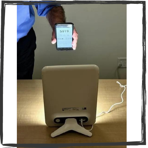A man holds his phone w/the lux measurement app active in front of a small, desk-based light box