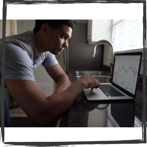 A young man sits in front of a laptop. On the screen is a moving average chart.
