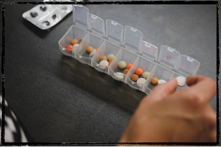 Photo of a hand placing a pill in a plastic carrier full of multi-colored pills