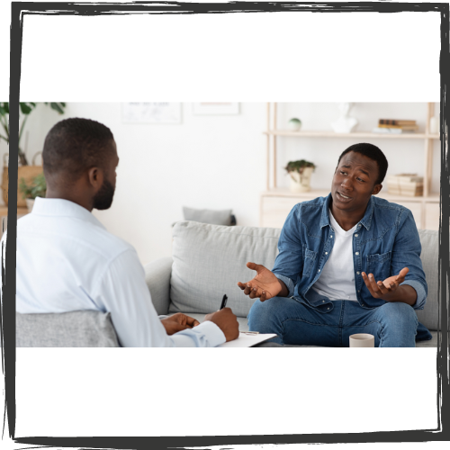 A Black male therapists talks to a Black male patient in an office