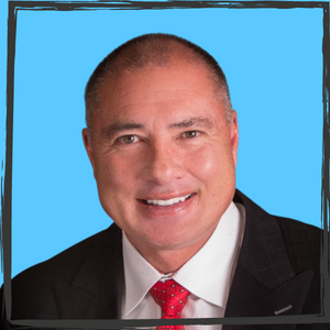 A smiling man with very short hair in a suit with a red tie