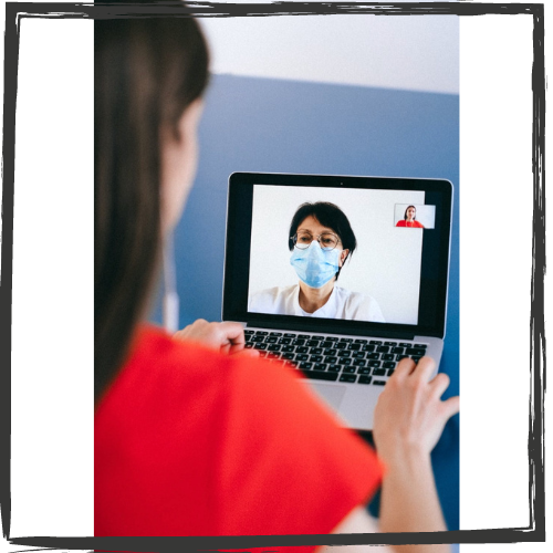 A woman w/long, black hair talks to a doctor on screen who wears glasses and a face mask 