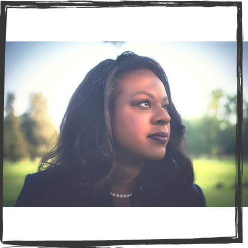 A Black woman w/shoulder-length dark hair and wearing a pearl necklace looks to the right; in the background are grass & trees