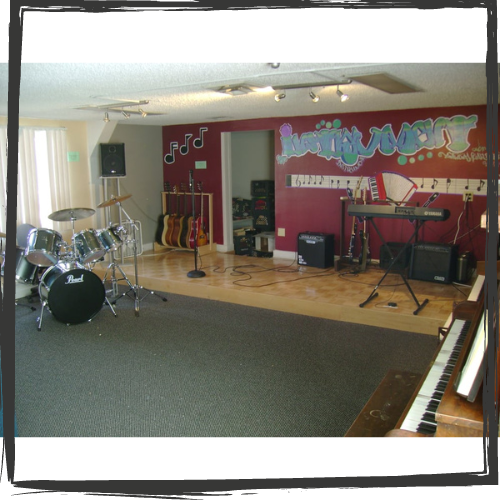 Photo of a room with a dark red wall, painted with grafitti-type art, a gray carpet and various instruments, including a drum set, keyboard, guitars , a microphone & amplifiers 