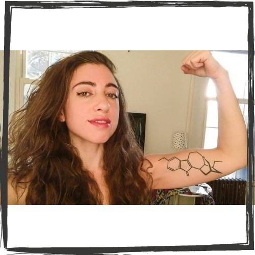 A young woman with long, brown hair curls her left arm in the air; on it is a tattoo of the formula for ibogaine