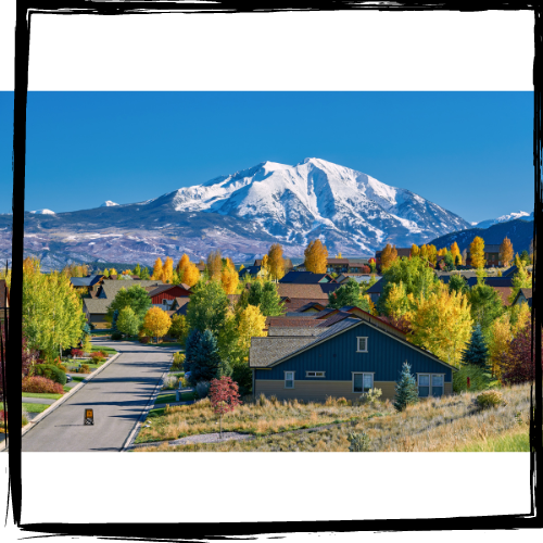 Photo of a 2-story house surrounded by trees in a neighborhood; in the background is a snowy mountain