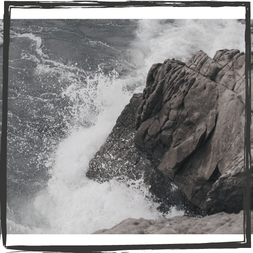 Photo of a gray, rock cliff with waves crashing onto it