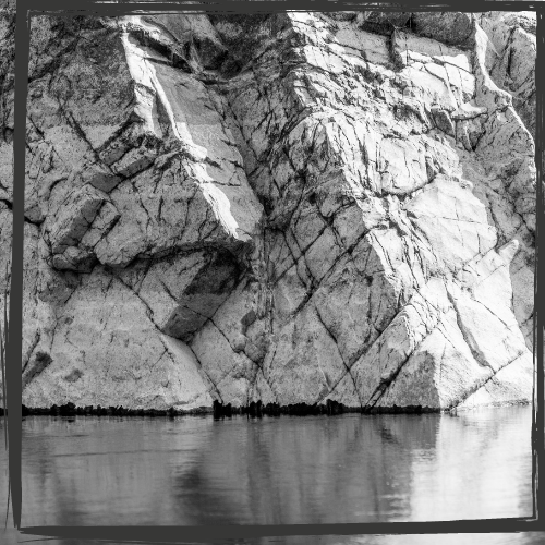 Black-and-white photo of a huge rock face reflected in water