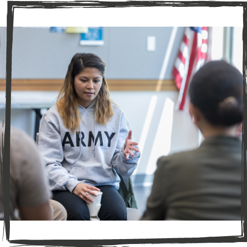A woman with shoulder length hair wearing a gray sweatshirt with "ARMY" on it speaks and gestures in a group