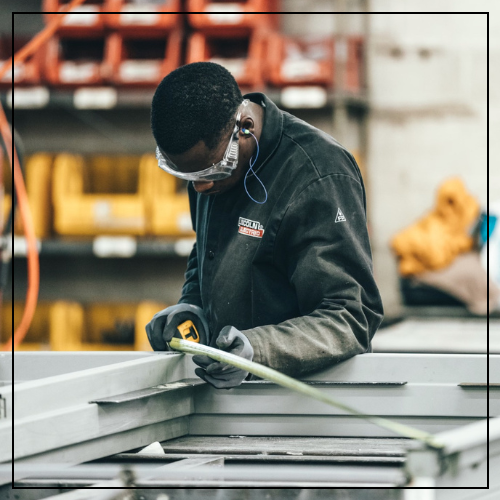 Photo of a Black, male factory worker looking down & measuring pieces of metal