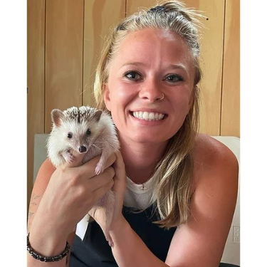 Photo of a young, blonde woman smiling and holding a hedgehog