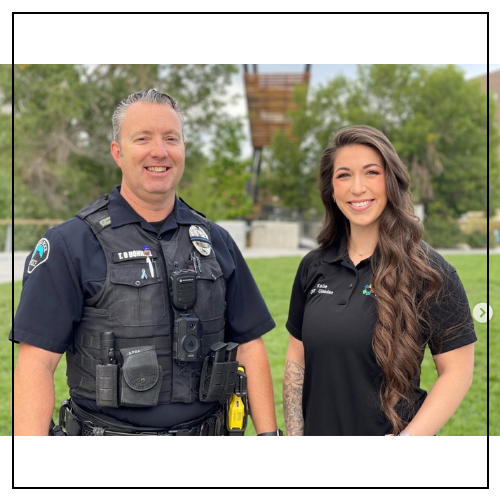 A white male police officer stands next to a white female therapist in a park